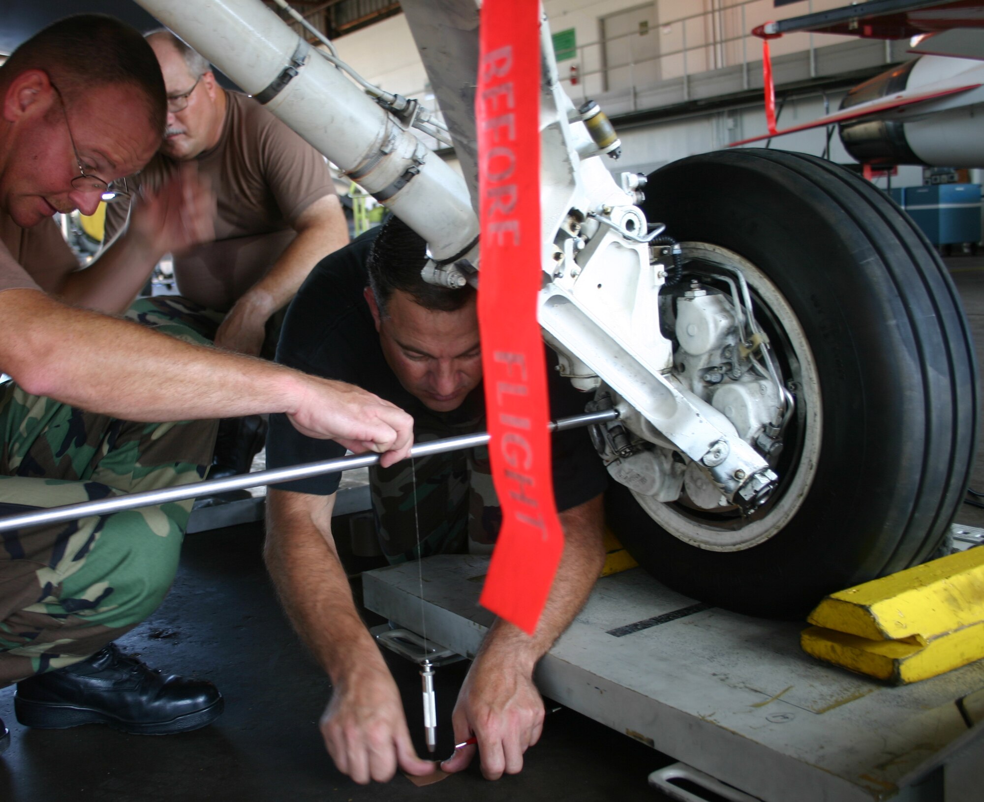 Tech. Sgt. Kevin Richmond of Whiteman Air Force Base, Mo., and Master Sgt. Chris Liszewski of the Maryland Air National Guard establish a plumb line from the rear landing gear to make an "x" on the floor while Master Sgt. Lewis Godfrey of the Air Force Reserves looks on. They do this on both of the rear gears and place a chalk line between the marks as part of the balancing an aircraft. (U.S. Air Force photo/Robert Fox)