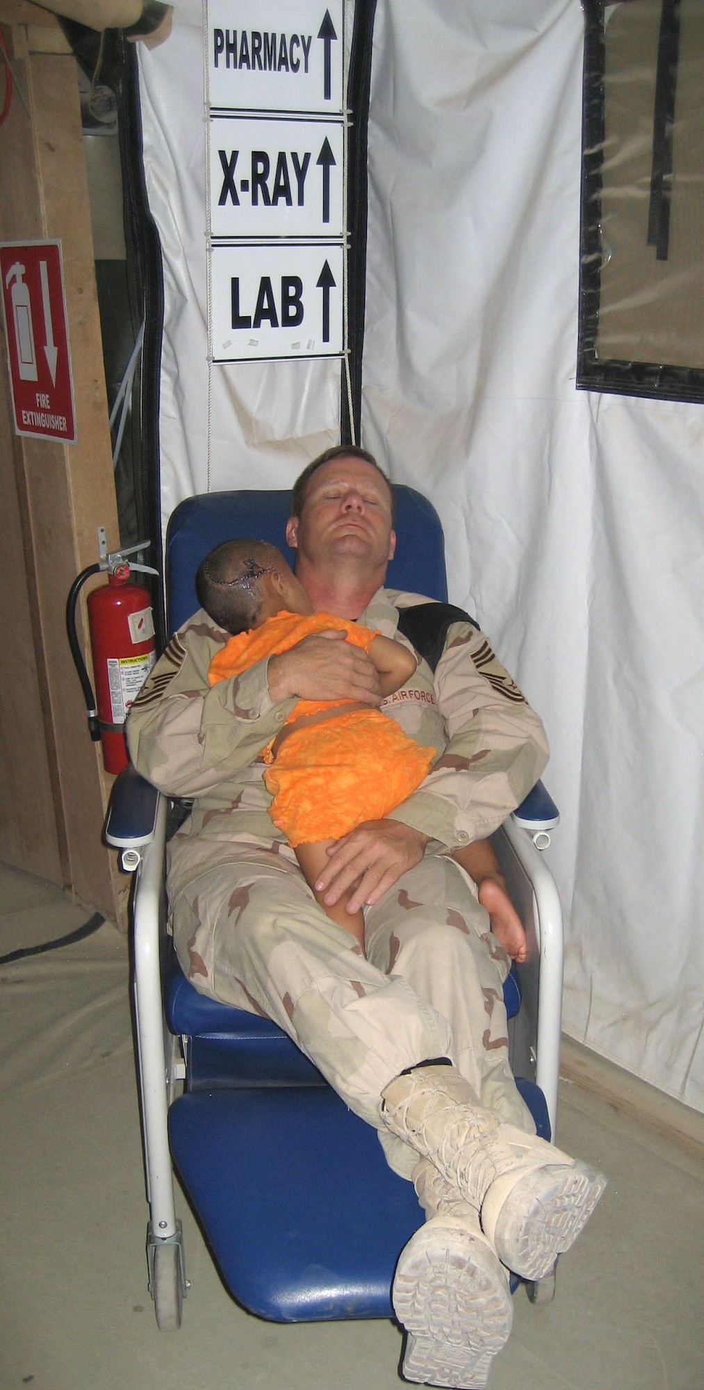 Chief Master Sgt. John Gebhardt cradles a young Iraqi girl as they both sleep in the hospital. The girl's entire family was executed by insurgents. The killers shot her in the head but she survived. The girl received treatment at the U.S. military hospital in Balad, but cries often. According to nurses at the facility, Chief Gebhardt is the only one who can calm down the girl, so he holds her at night while they both sleep in a chair. Chief Gebhardt was assigned to the 332nd Expeditionary Medical Group at Balad Air Base, Iraq. (Courtesy Photo)