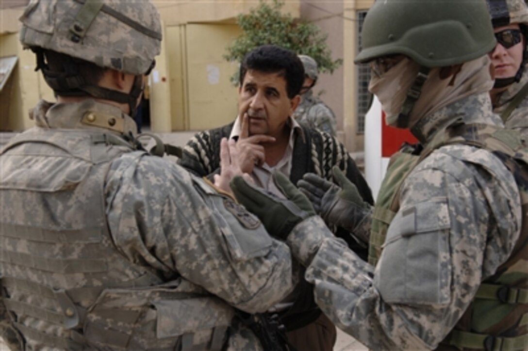 A U.S. Army soldier (left) from the 4th Battalion, 14th Cavalry Regiment, 172nd Stryker Brigade Combat Team speaks to a city council member (center) about a food delivery with the help of an interpreter during a medical and humanitarian mission in Baghdad, Iraq, on Nov. 9, 2006.  