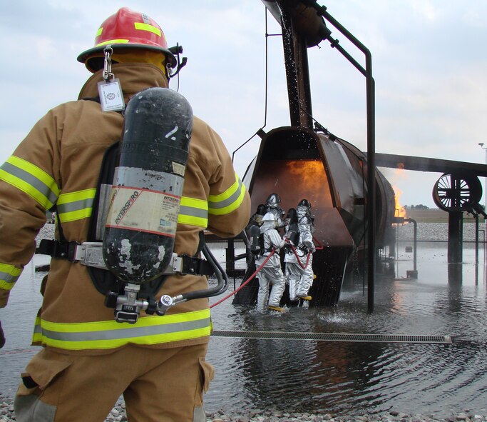 (Photo by Capt. Tony Wickman) A Vance firefighter watches Colonel Benson lead the charge into the burning aircraft to douse the 1,800-degree fire. Within minutes, the flames were extinguished.