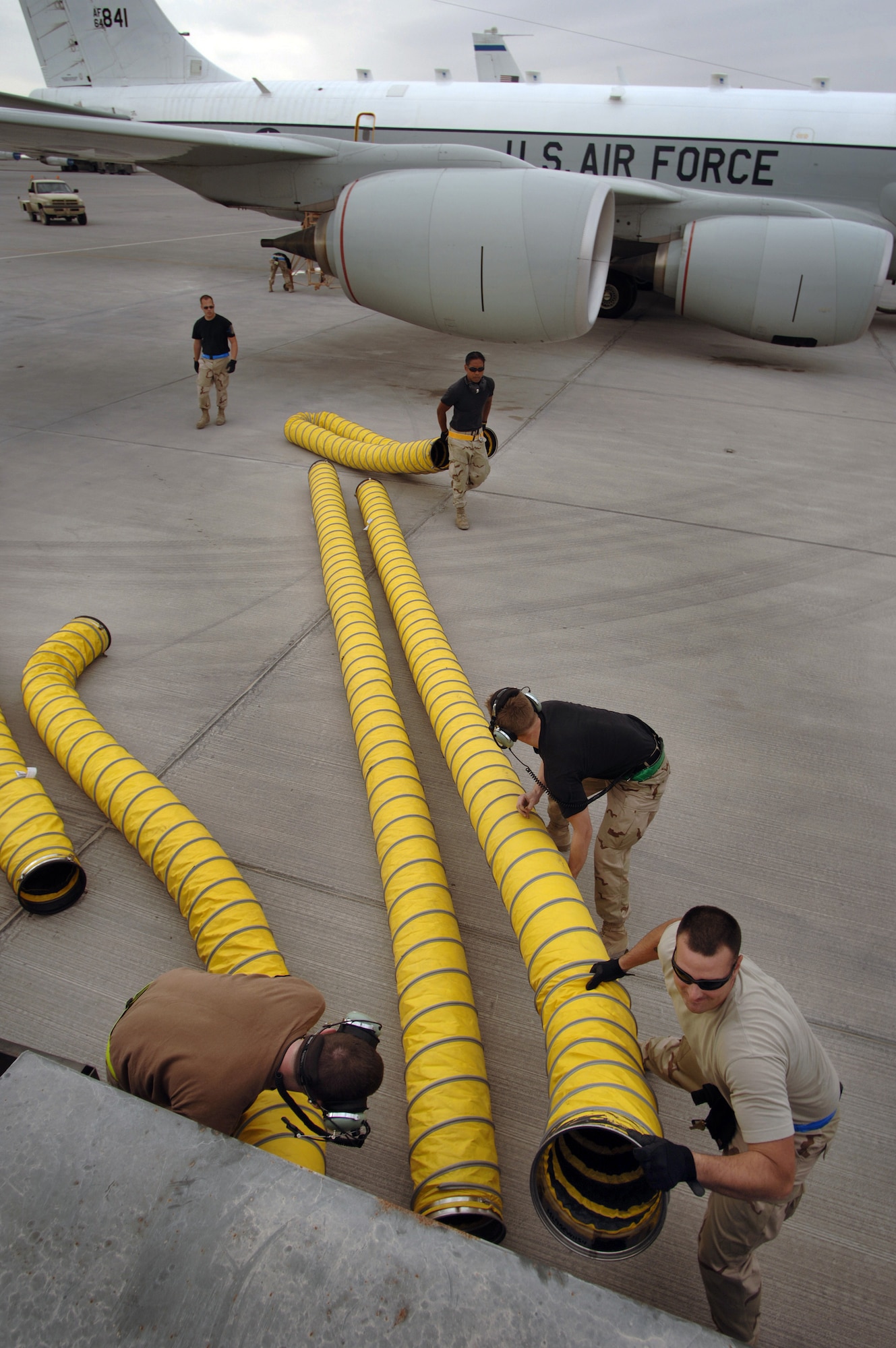 After the removal of air conditioning hoses that were connected to an RC-135 Rivet Joint reconnaissance aircraft, Staff Sgt James Scott assists crew chiefs in stowing them away prior to the plane's departure for a mission over Southwest Asia. The hoses help maintain cool temperatures for the extensive inventory of electronics aboard the plane during its lengthy start up process. Sergeant Scott is a life support technician deployed from the 343rd Reconnaissance Squadron and the crew chiefs are from the 55th Aircraft Maintenance Squadron from Offutt Air Force Base, Neb. (U.S. Air Force photo/Master Sgt. Scott Wagers)
