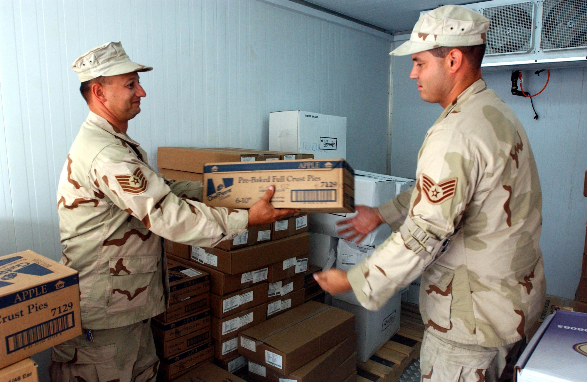 Tech. Sgt. Charles Allegretta hands Staff Sgt. James Lotz a case of apple pies that will be baked for the Thanksgiving feast. More than 130 pies were ordered in all flavors -- pumpkin, sweet potato and pecan included. (U.S. Air Force photo/Master Sgt. Jason Tudor)
