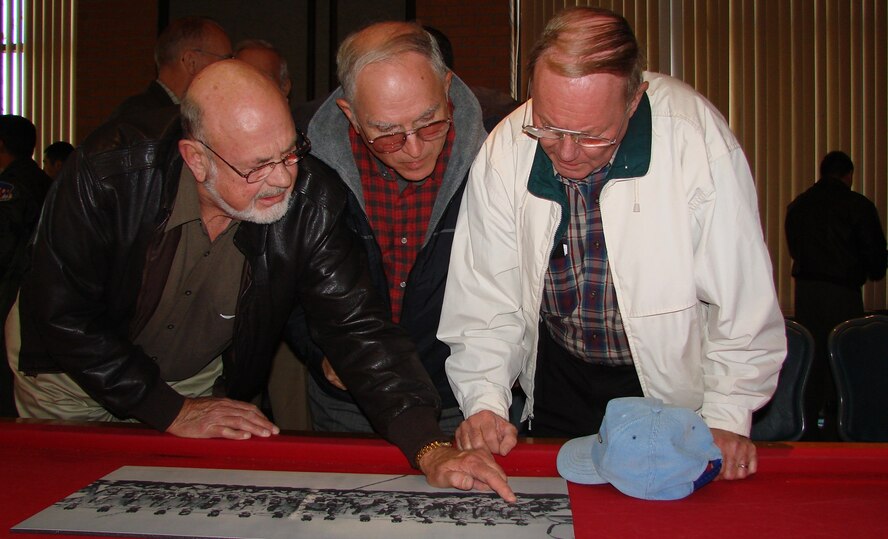 (Photo by Frank McIntyre) Richard Trumbly, Norm Parkhurst and Bob Steeneck try to identify other class members in Class 62-F’s graduation photo. The three and 40 other classmates were the first to train in the T-37 at Vance Air Force Base. Several class members attended the Oct. 27 T-37 departure ceremony.