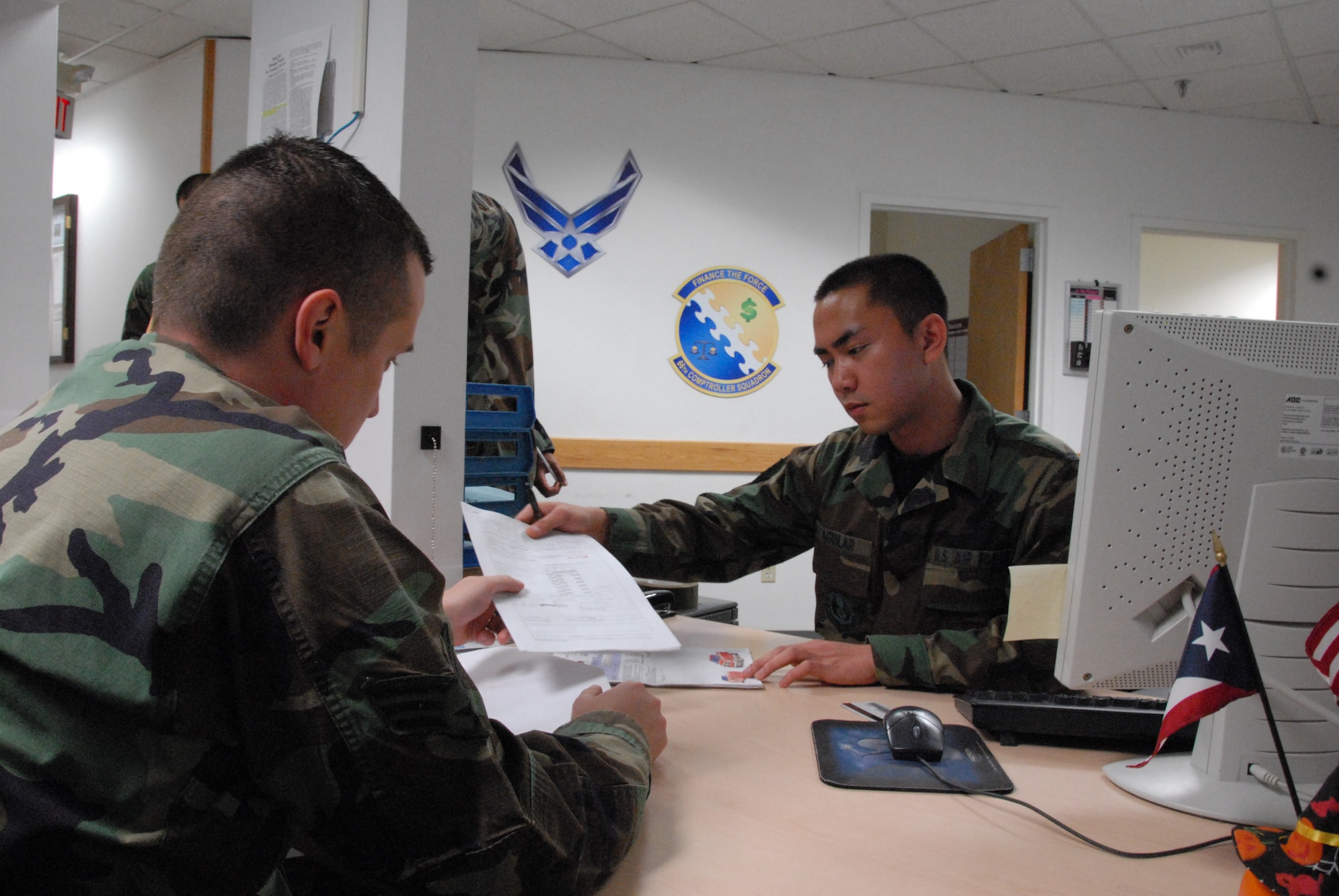 From left, Senior Airman Jeremy Meier, 66th Comptroller Squadron, receives help from Airman 1st Class James Aguilar, 66 CPTS, with a travel voucher. Photo by Airman 1st Class Clinton Atkins