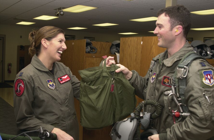 (Photo by Frank McIntyre) Capt. DeAnna Franks hands her husband, Capt. Tony Franks, his pilot bag before a flight. Both husband and wife are Vance instructor pilots.