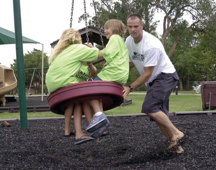 (Photo by Capt. Paula Bissonette) Camp Tomahawk 2004 participants get pushed by Capt. Jeremiah Gentry, 2004 Camp Tomahawk volunteer, on a swing at the base park. Forty underprivileged children are scheduled to attend this year’s two-week camp.