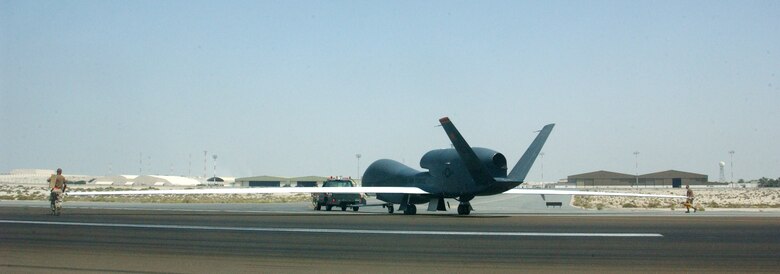 Airmen from the 12th Reconnaissance Squadron and 380th Expeditionary Maintenance Group tow a Global Hawk unmanned aerial vehicle back to its hangar after a mission Oct. 3 at a deployed location in Southwest Asia. The Global Hawk can survey large geographic areas with pinpoint accuracy to give military decision-makers the most current information about enemy locations, resources and members. (U.S. Air Force photo/Master Sgt. Jason Tudor)