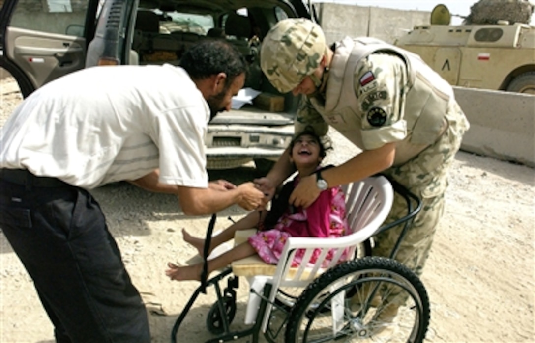 An Iraqi man and Polish army Maj. Peter Lewandowski, assigned to the Civilian Military Cooperation Unit, strap the man's disabled daughter into her new wheelchair at Camp Echo, Iraq, Oct. 3, 2006.  The Polish CIMIC funds, contracts, and inspects projects. 