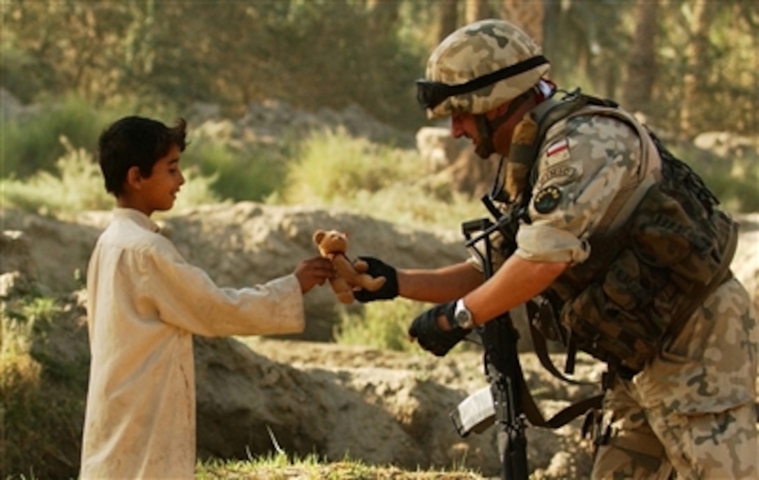 Polish army Lt. Col. Andrzej Kujawa, Civil Military Cooperation Group commander, gives a small teddy bear to a young local boy during a project completion visit in Al Bufriha, Iraq, Sept. 30, 2006. The Polish CIMIC funds, contracts, and inspects projects designed to help revitalize Iraq's economy and provides supplies and services to Iraqi army soldiers and civilians. 