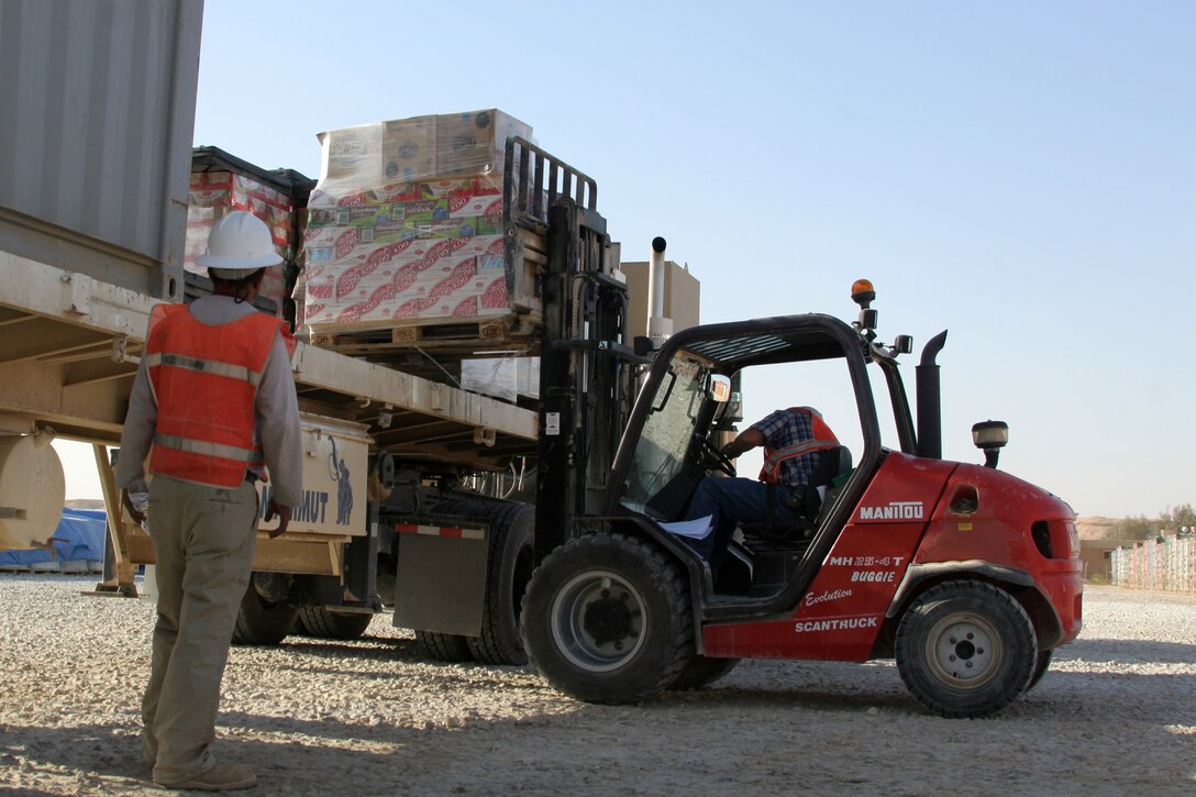 A third-country national watches Mark Neeley as he loads a pallet of packaged food items onto a trailer at Al Asad, Iraq, Oct. 5. Neeley is a logistics warehouseman with Corps Logistics Support Services, Kellogg, Brown and Root. He is a native of Belton, Texas.
