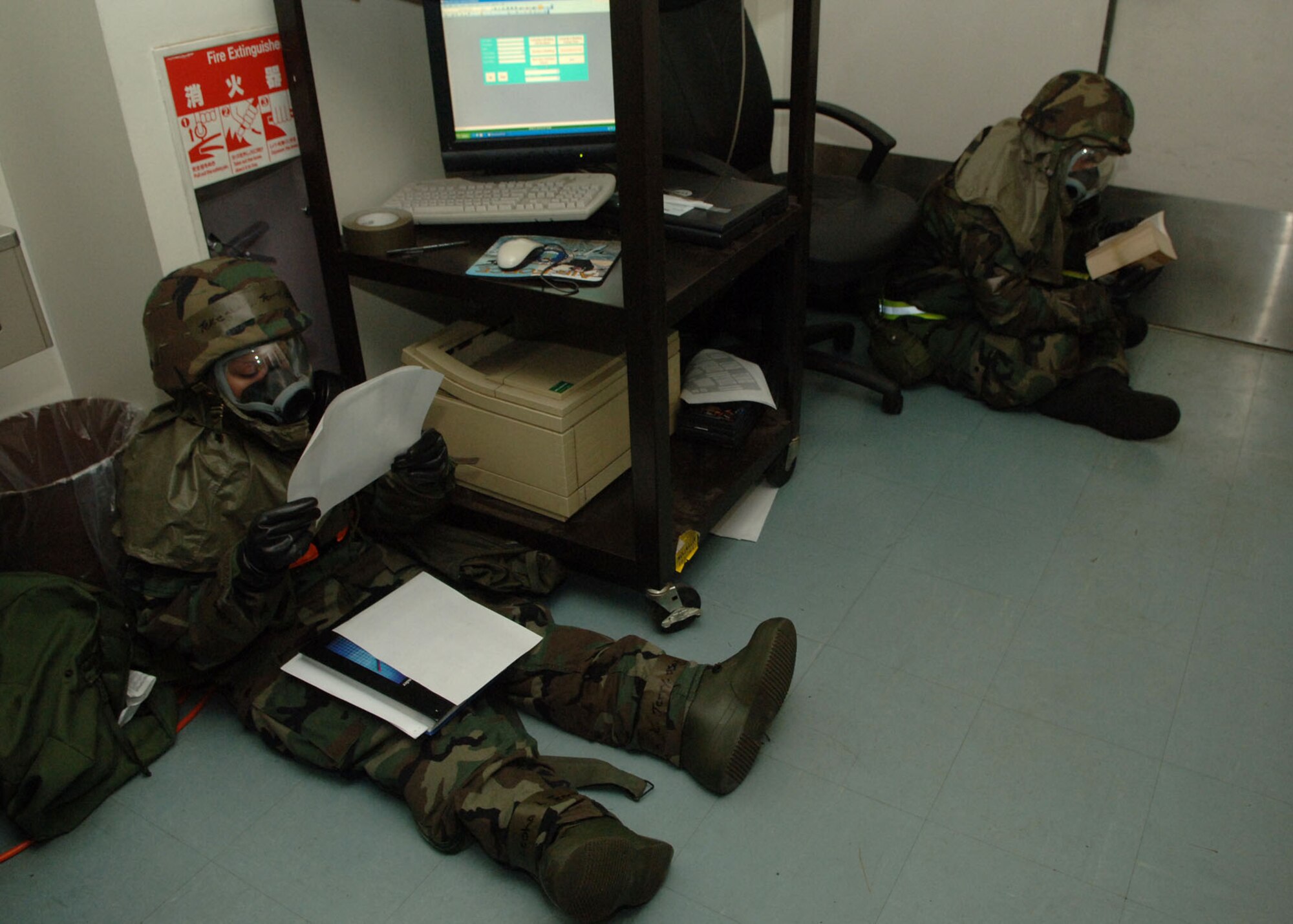 Staff Sergeant Tekesha Terry and Airman 1st Class Thomas Underwood read while in mission-oriented protective posture 4 at Yokota Air Base, Japan, during a simulated attack that was part of a 374th Air Wing exercise. MOPP levels relate to chemical or biological hazards.  Both Airmen are with the 36th Airlift Squadron. (U.S. Air Force photo/Senior Airman Veronica Pierce)