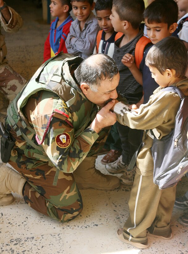 Major Gen. Tariq Abdul Wahab Jasin, Commanding General of the 1st Iraqi Army Division kisses the hand an Iraqi student of Al Madinah School during a civil affairs mission in Al Madinah As Siyahiyah (Tourist Town), Iraq, October 9. Marines with 4th Civil Affairs Group, 1st Marine Expeditionary Force (Forward), and soldiers with Able Company, 2nd Combined Arms Battalion, 136th Infantry Regiment, 1st Marine Logistics Group (Forward), accompanied Tariq and the Iraqi Army to visit a recently opened school in Tourist Town and distribute supplies to the children. During the visit, the Iraqi Army soldiers handed out school materials and the school principal accepted a $500 donation from the families of soldiers with 2nd Combined Arms Battalion to assist with the moving costs to their new building and any other expenses. The check was presented to the principal by Army Lt. Col. Gregg L. Parks, Battalion Commander of 2nd Combined Arms Battalion accompanied by Tariq.