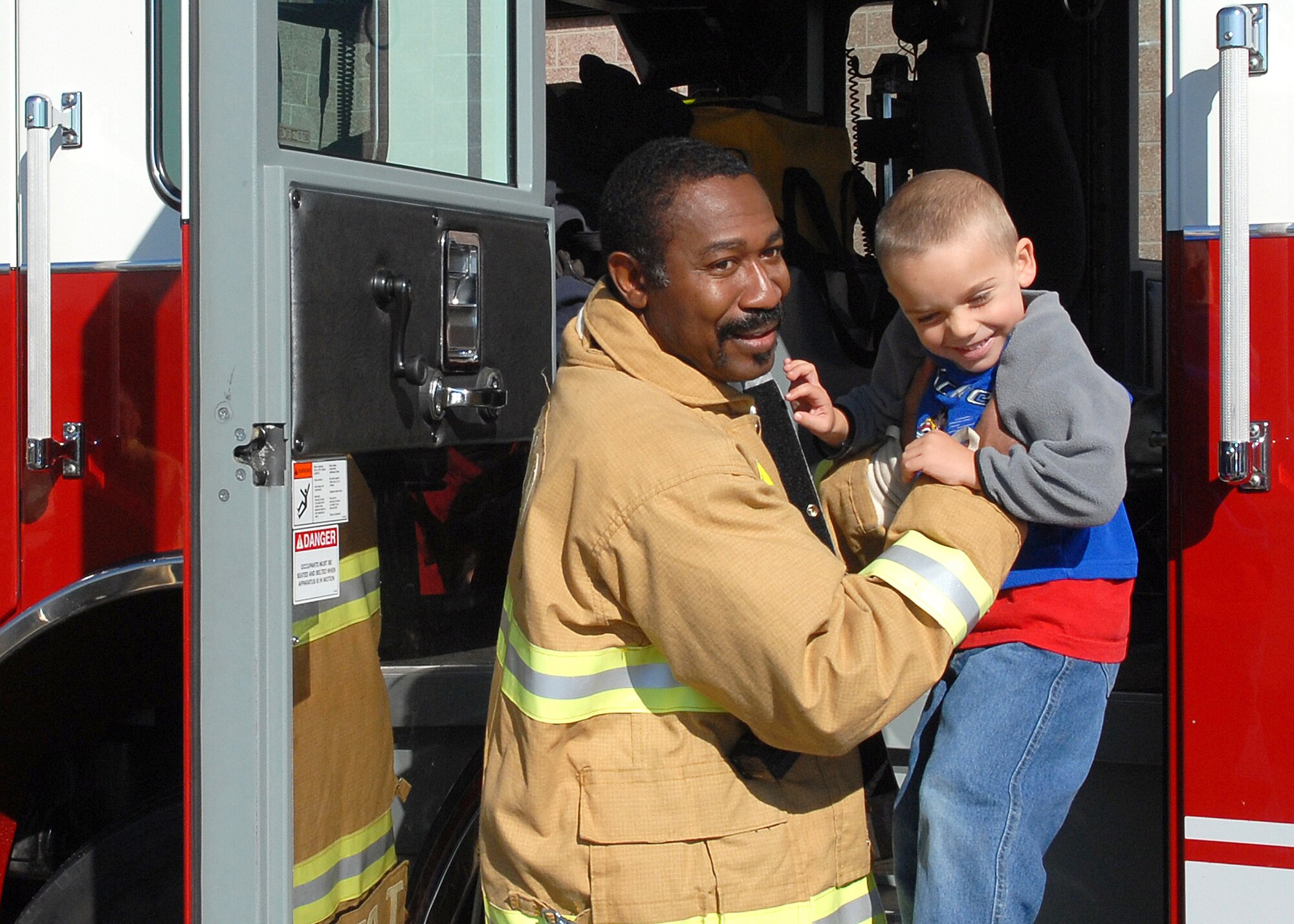 BUCKLEY AIR FORCE BASE, Colo. -- Fire Fighter Thomas Bryant lowers three-year-old Davian Mora from a firetruck during the fire department's visit with their mascot, Sparky the Fire Dog, to the Child Development Center here Oct. 12. The visit was to inform children about fire saftey and show them their equipment. Visiting the CDC was one of the events planed for Fire Prevention Week on the base. (U.S photo by Senior Airman Steve Czyz)