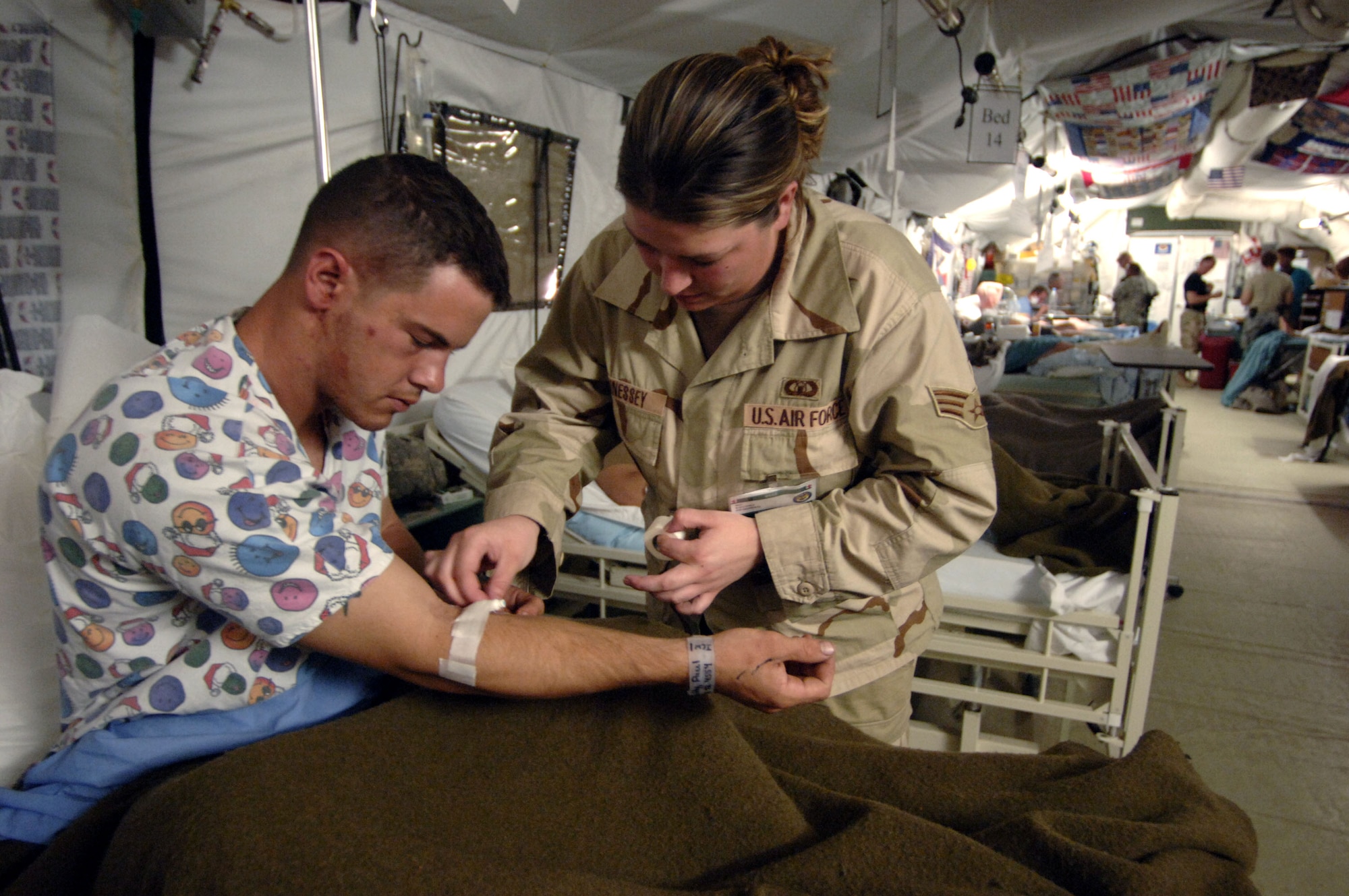 During her day off from work, Senior Airman Jamie Hennessey applies tape to an IV drip line in the arm of Army Specialist Paul Smithy who was wounded in a blast near Balad, Iraq.  When not in the tower as an air traffic controller, she works as a volunteer at the Air Force Theater Hospital at Balad Air Base, Iraq.  (U.S. Air Force photo/Master Sgt. Scott Wagers)