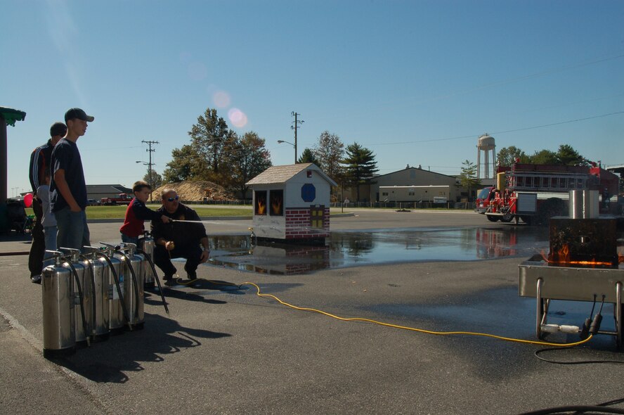 Thomas Morris, son of David Morris, 436th Civil Engineer Squadron, extinguishes a propane fire with water with the help of Barry Williams, 436th CES firefighter, during the 436th CES Fire Department's Open House at the base fire station here Saturday. (U.S. Air Force photo/Staff Sgt. James Wilkinson)