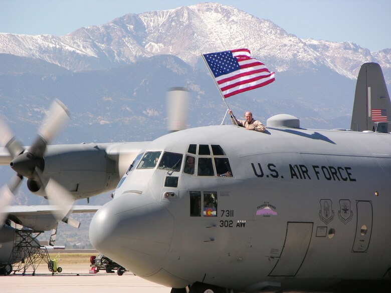 PETERSON AIR FORCE BASE, Colo. (AFRC) -- Maj. Stephen Stelly, 731st Airlift Squadron flight commander, proudly displays the American flag as a 302nd Airlift Wing C-130 taxis past Pikes Peak during a recent homecoming. On Oct. 4, wing members ended 14 months of deployments in support of U.S. Central Command operations in Southwest Asia. (U.S. Air Force photo by Master Sgt. Mark Clark)