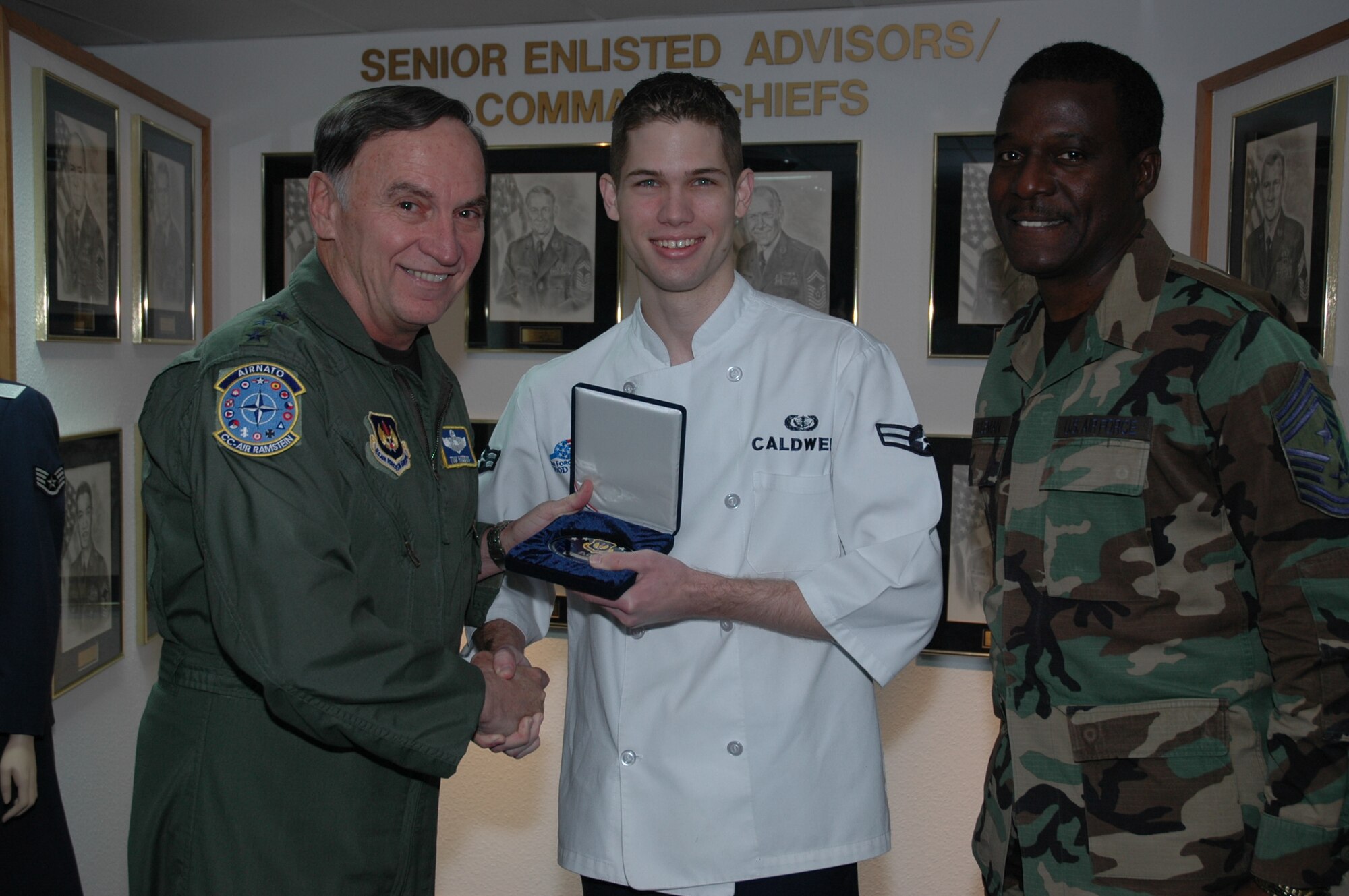 Gen. Tom Hobbins, U.S. Air Forces in Europe commander (left), and Chief Master Sgt. Gary G. Coleman, USAFE command chief master sergeant (right) present an Airmen Committed to Excellence coin Oct. 17 to A1C Nickolas Caldwell at a surprise ceremony in the Parish Enlisted Heritage Room. The ACE award consists of a large medallion engraved with the recipient's name and sequentially numbered by order. (U.S. Air Force photo/Master Sgt. Chuck Roberts)