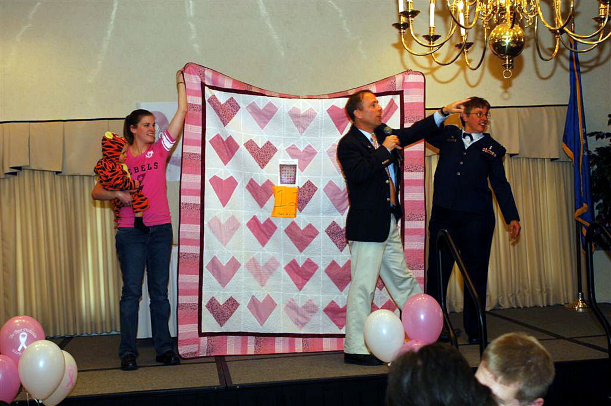 Bill Large, from the 5th Medical Support Squadron, auctions off a quilt called "Hearts for a Cure" during the quilt auction for the National Breast Cancer Awareness Month event at Minot Air Force Base, N.D., Oct. 24, while the makers of the quilt -- Rebecca Ament and Lt. Col. Anne Heinly, 5th Medical Operations Squadron commander -- hold it up. All proceeds from the auction, which raised almost $4,000, were donated to breast cancer research through the Combined Federal Campaign. The event, themed "Voices of Breast Cancer, Inspiring Hope, Supporting a Cure, included a health fair and the personal testimony of several breast cancer survivors from the base community. Photo By: Airman First Class Cassandra Butler