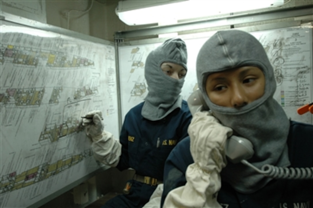 U.S. Navy Seaman Sandra Rodriguez receives damage control information over the phone as Ensign Ashley Lorenz plots the simulated damage during a general quarters drill aboard the amphibious assault ship USS Boxer (LHD 4) on Oct. 19, 2006.  Rodriquez and Lorenz wear long gloves and balaclavas to protect them from flash fires.  