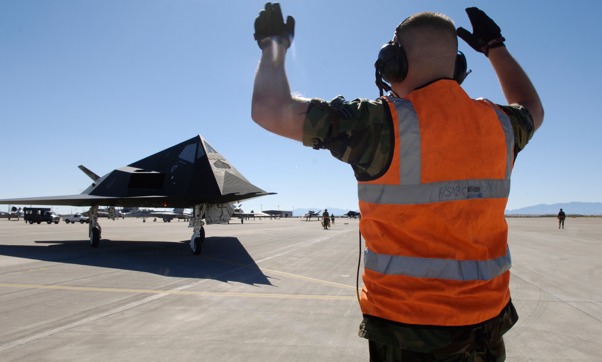 Senior Airman Justin Byars marshals in an F-117 Nighthawk for an end of runway inspection before takeoff from the Holloman Air Force Base N.M. The stealth fighter was one 25 Nighthawks that flew in a formation celebrating the plane's 25th Anniversary. Airman Byars is a crew chief with the 49th Aircraft Maintenance Squadron. (U.S. Air Force photo/Senior Airman Brian Ferguson)