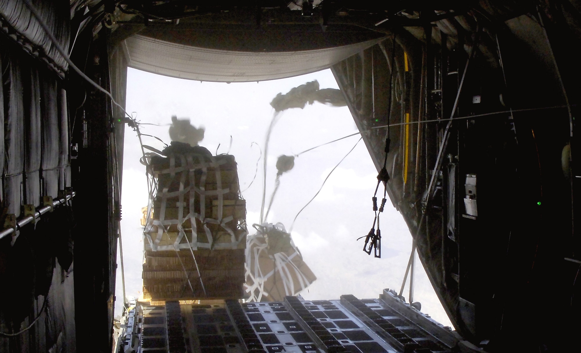 Joint Precision Air Drop System bundles fall out of the back of a C-130 Hercules Aug. 25. The drop was made from almost 10,000 feet above sea level and was calculated using up-to-the-minute wind data relayed from two small dropsondes deployed 20 minutes earlier. The dropsondes calculate wind speed and relay the information back to the aircraft, helping to calculate the correct drop point. (U.S. Air Force photo/Senior Airman Brian Ferguson) 