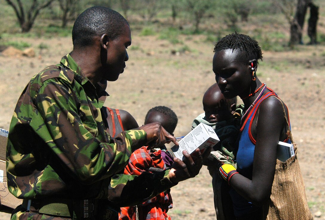 A Kenyan army soldier explains the directions on a box of medication to a Pokot mother after she