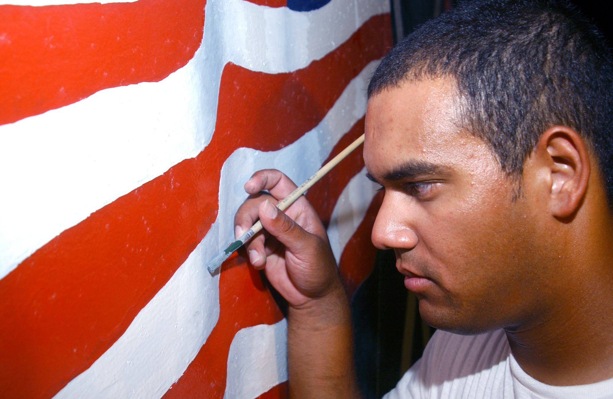 Senior Airman Osvaldo Ros-Henriquez paints details on an American flag Sept. 7, part of a design for a stage recently constructed for the 380th Expeditionary Wing at a forward-operating base in Southwest Asia. Airman Ros-Henriquez was part of a group of people who won a design contest after the stage was built. The work, which includes the U.S. Central Command Air Forces and wing crest, took about three weeks to complete. Airman Ros-Henriquez is assigned to the 380th Expeditionary Civil Engineer Squadron. (U.S. Air Force photo/Master Sgt. Jason Tudor)