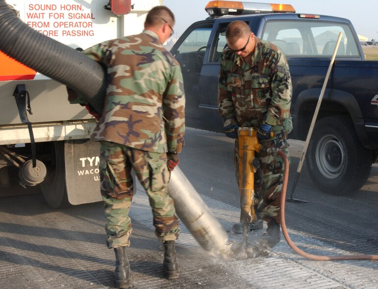MINOT AIR FORCE BASE, N.D. -- Staff Sgt., Neil Crawn, 5th Civil Engineer Squadron, hammers-out decayed parts of the runway as Staff Sgt, Joe Walkup, 5th CES, uses a suction tube to vacuum smaller rocks as part of the yearly runway repair, Wednesday.(U.S. Air Force photo by Airman First Class Joe Rivera)