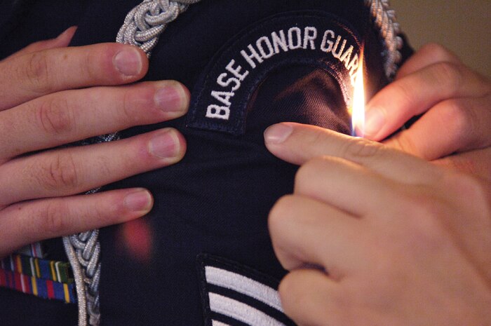 Airman 1st Class Timothy Young, 437th Aircraft Maintenance Squadron, uses a lighter to burn a loose string from the ceremonial service dress uniform of Staff Sgt. Michael Fronk, 437th Communications Squadron,  as they prepare for a funeral. (U.S. Air Force photo/Senior Airman Desiree N. Palacios)