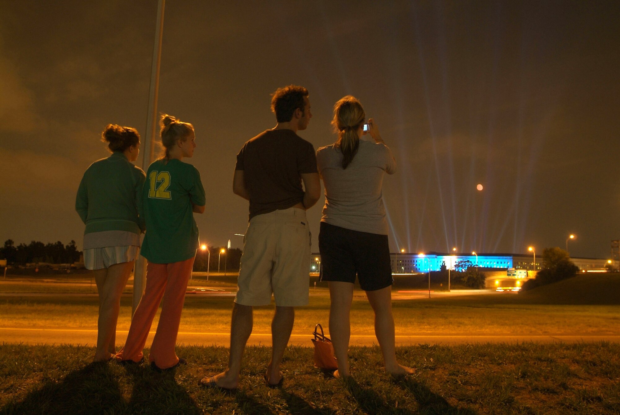 Arlington, Va., resident Allison Bacon (right), who works for Navy Facilities Engineering Command at the Washington Navy Yard, takes a picture of the 184 beams of light emanating from the Pentagon courtyard as Hillary Hout (from left), Melissa Twardzik and Chris Tassa look on. The lights commemorate each life lost during the Sept. 11, 2001, attack on the Pentagon. (U.S. Navy photo/Chief Mass Communication Specialist Mate Johnny Bivera)
