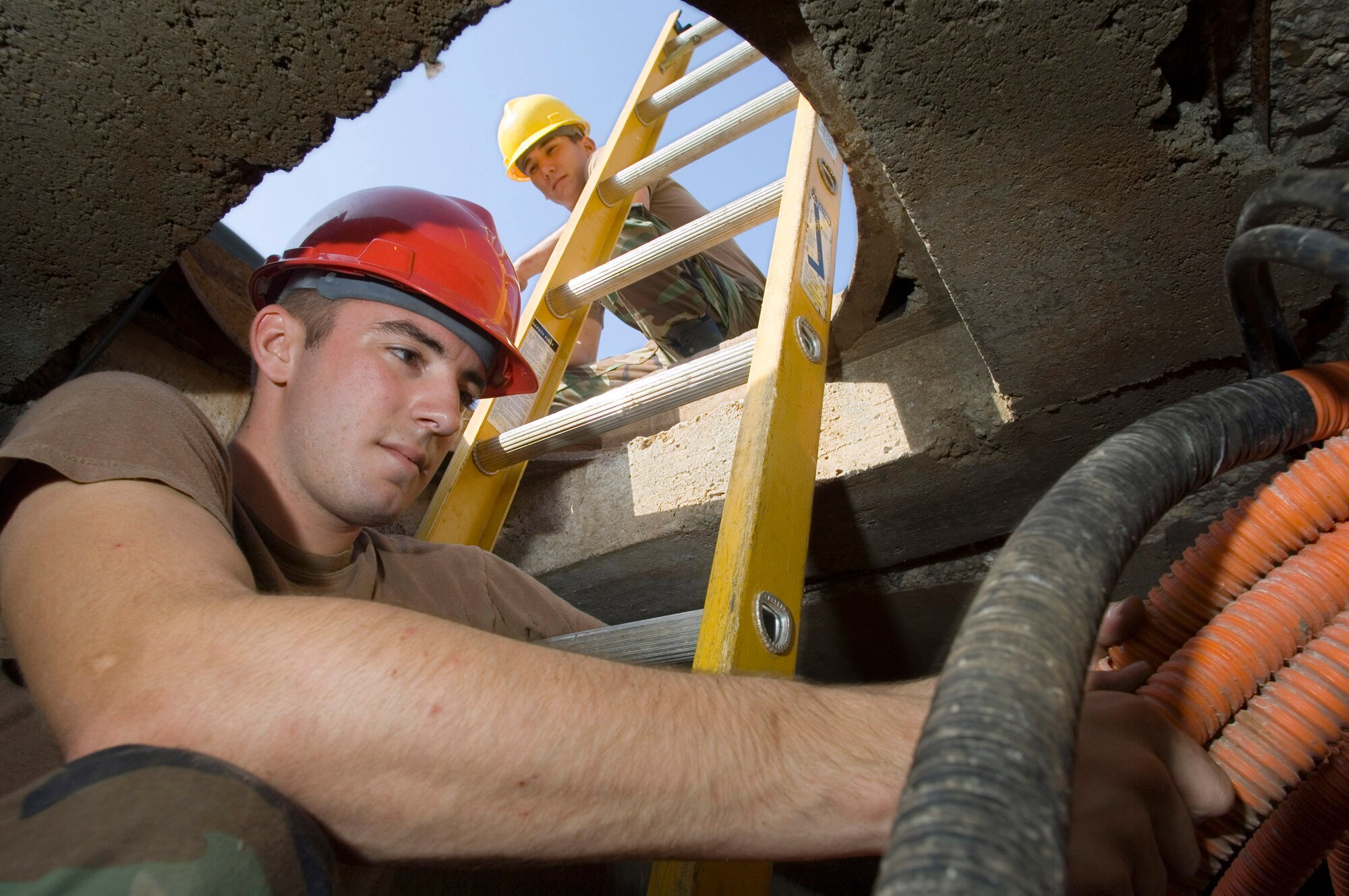 Airman 1st Class Jeremi Welborn searches for a fiber optic cable as Airman Kenneth Townsend waits to assist outside a manhole at Ramstein Air Base, Germany, Sept. 11, 2006. They are cable maintainers with Ramstein's 435th Communications Squadron. (U.S. Air Force photo/Master Sgt. John E. Lasky)