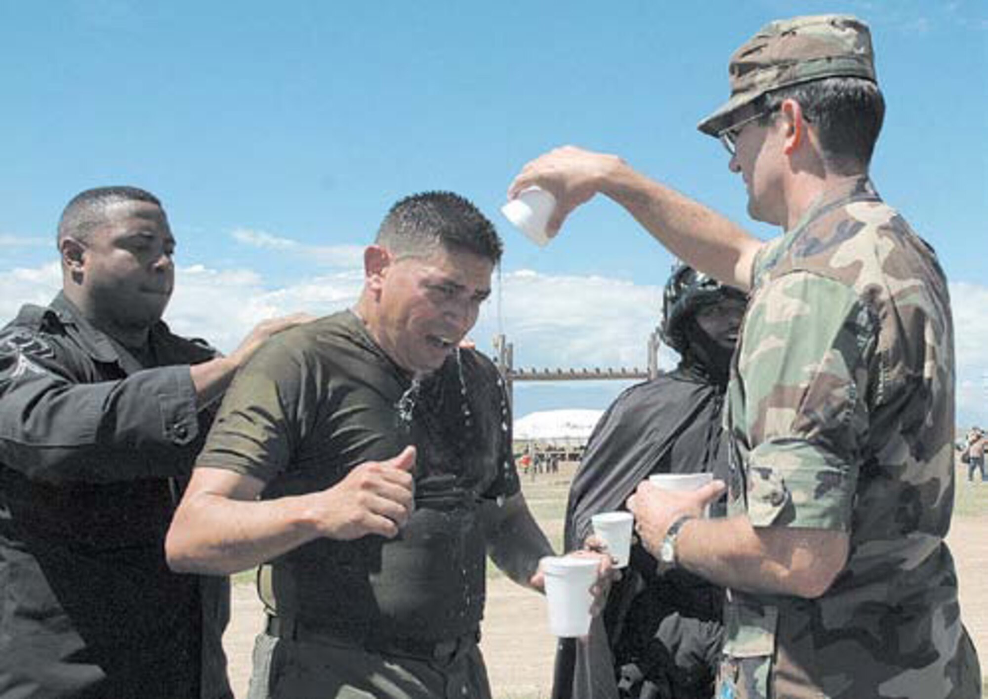 Col. Joseph Schwarz (right), 61st Air Base Wing commander, cools down Cpl. Manuel Rodriguez (center) after his completion of the obstacle course in the heat of the day at high altitude. Cpl. Michael Hill (left) pats Corporal Rodriguez on the back as the SMC Mascot, Lorenzo Humphrey, cheers them on.