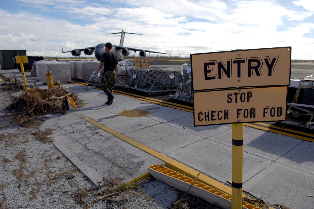 An Airman walks past pallets lined up on the Wake Island flightline Sept. 12, which were offloaded from the C-17 Globemaster III in the background. The 36th Contingency Response Group at Andersen Air Force Base, Guam, is assisting a 53-person team from Hickam AFB, Hawaii, assessing damage left by Super Typhoon Ioke after it hit the island Aug. 31. (U.S. Air Force photo/Tech. Sgt. Shane A. Cuomo)