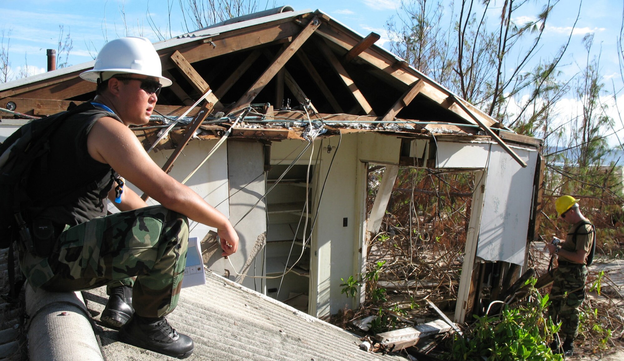 Staff Sgt. Song Lee sits on a displaced roof while Tech. Sgt. Dennis Tye prepares to take a photo f the wreckage at Wake Island Sept 15, 2006 . Both Airmen work for the 15th Civil Engineering Squadron and were sent as part of the 15th Airlift Wing's Damage Assessment Team to estimate the cost of damage left by Super Typhoon Ioke. The category 5 storm blew across the atoll Aug 31 with 155 mph winds and 190 mph gusts. (U.S. Air Force photo / Tech. Sgt. Chris Vadnais)
