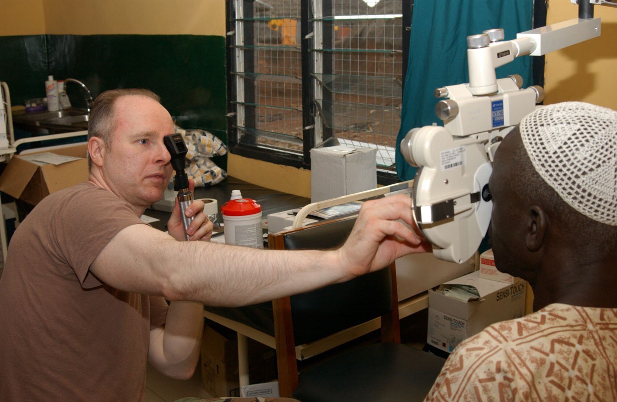 Maj. Craig McCluer, an optometrist from the 52nd Medical Group, Spangdahlem AB, Germany, does a basic eye exam on a Ghanaian man at the Bilpeila Clinic in Tamale, Ghana, during Med Flag 2006.  Major McCluer is one of more than 50 U.S. Air Forces in Europe personnel deployed to the West African city for the 10-day exercise where U.S. military personnel are working with their African military counterparts by staging medical operations in the countries of Benin, Senegal, Nigeria, and Ghana.   The Tamale mission includes medical field clinics in the remote city of Tampiong, and one at the edge of Tamale.  At both sites, local residents can see an optometrist, dentist, pediatrician or family care physician.  (Photo by TSgt Pamela Anderson)      