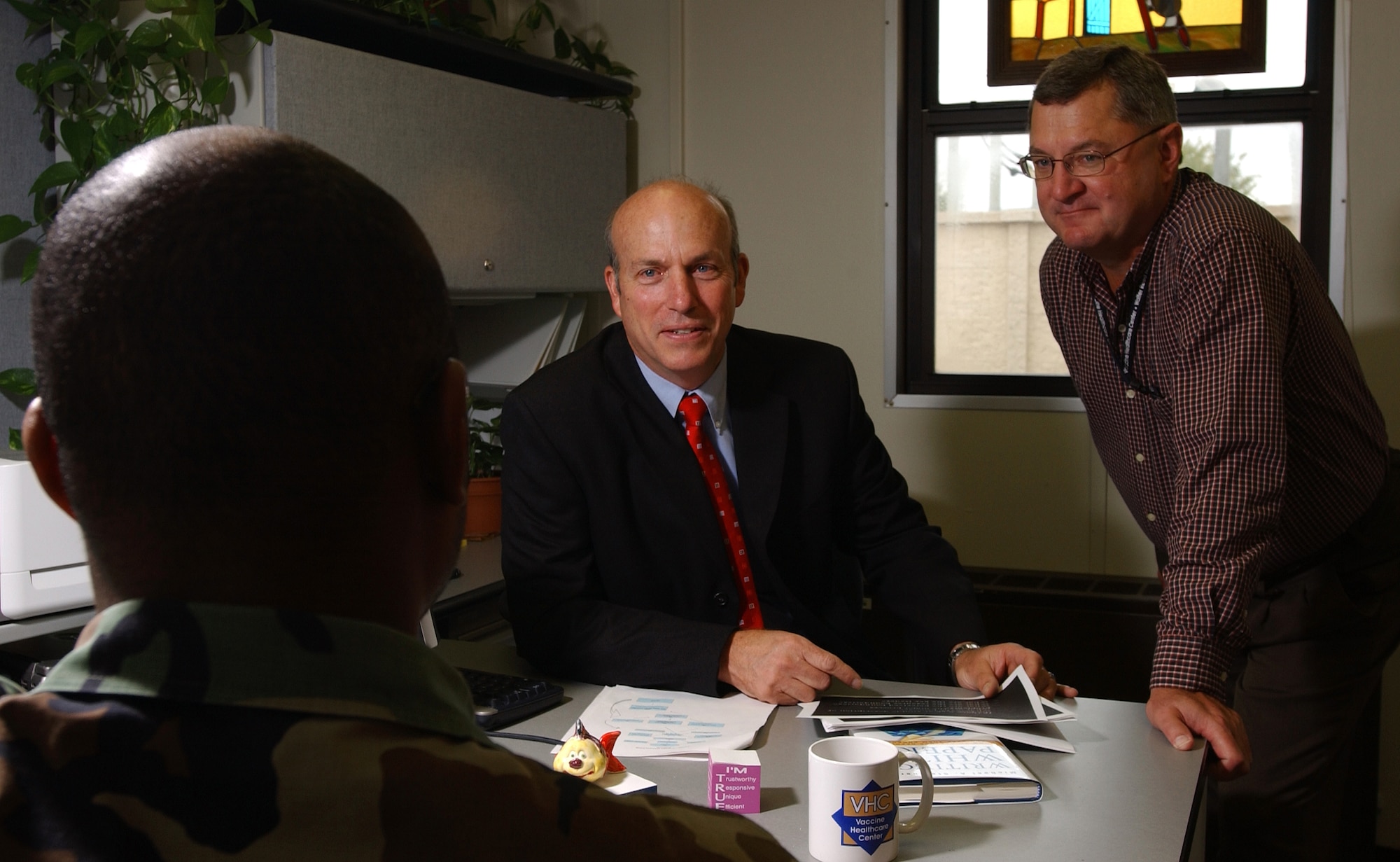 Vaccine Healthcare Center Network medical director Dr. David Hrncir (center) and Tom Rampy, the VHC health educator (right) discuss vaccine adverse reaction reporting with a military member at Wilford Hall Medical Center at Lackland Air Force Base, Texas. (U.S. Air Force Photo by Master Sgt. Kimberly Yearyean-Siers)