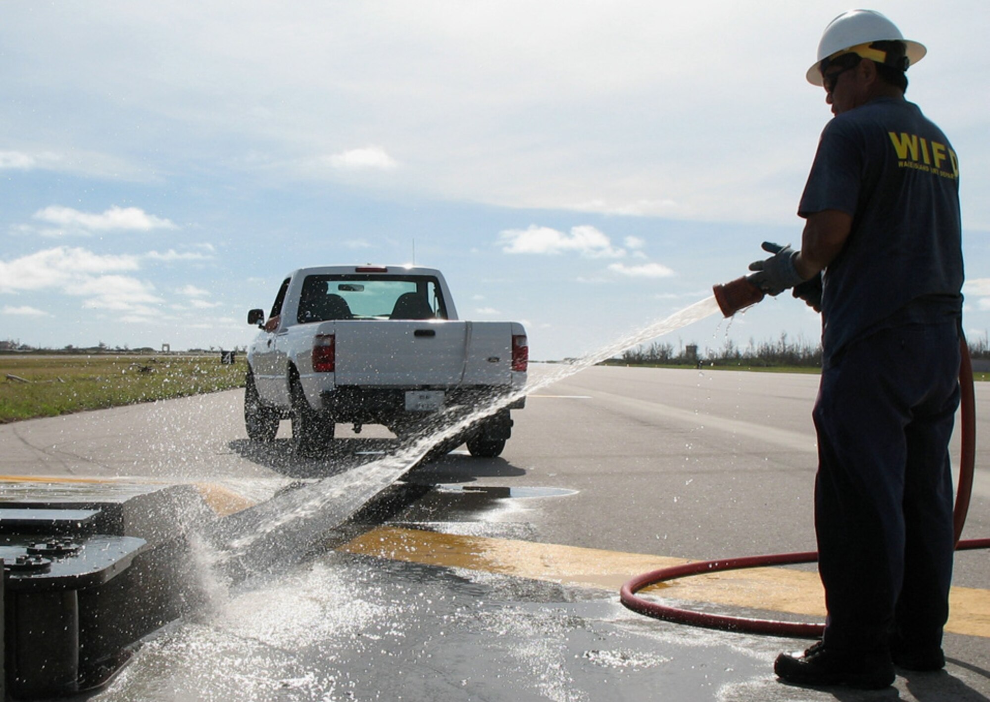 Thomas Hunter pulls a nylon strap from an aircraft arrest system while a firefighter rinses it off at Wake Island Sept. 20. (U.S. Air Force photo/Tech. Sgt. Chris Vadnais)