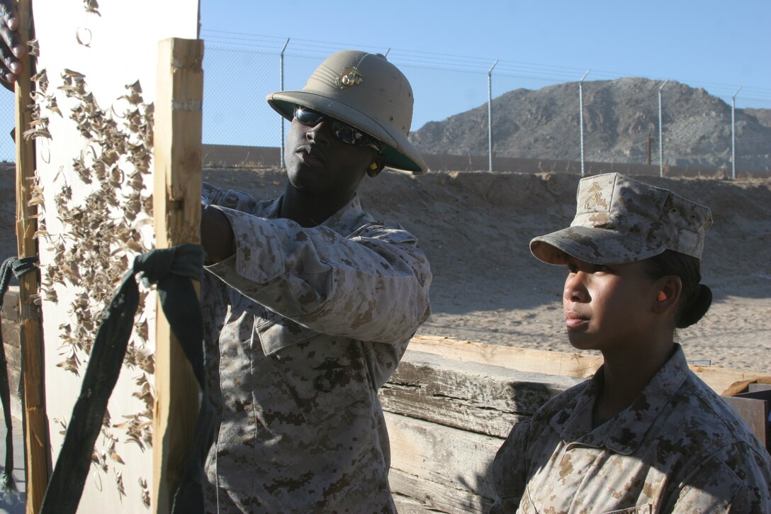 Sgt. Alexander Mobley, Range Safety Officer, inspects a target with Cpl. Judith Carver on the pistol range.