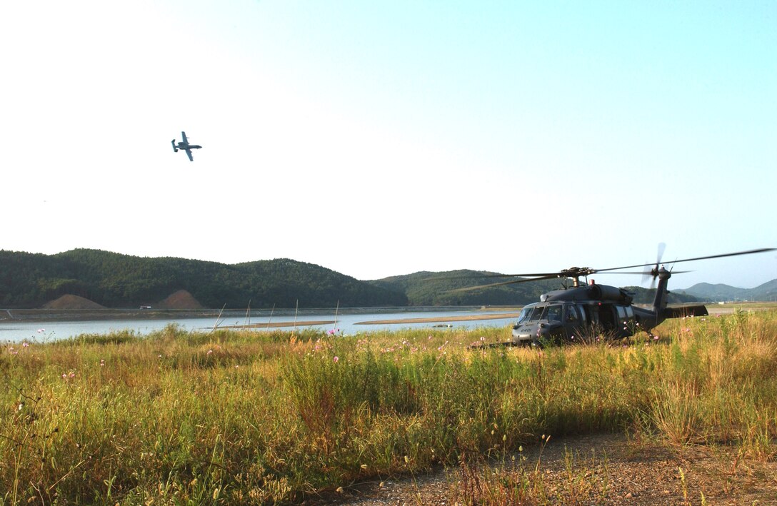 An HH-60 Pavehawk crew prepares to recover two survivors while an A-10 Thunderbolt II flies overhead during combat search and rescue training Sept. 21 near Osan Air Base, South Korea. Annual training is conducted by survival, evasion, resistance and escape instructors to reacquaint aircrew members with combat search and rescue procedures and techniques. (U.S. Air Force photo/Airman 1st Class Chad Strohmeyer)