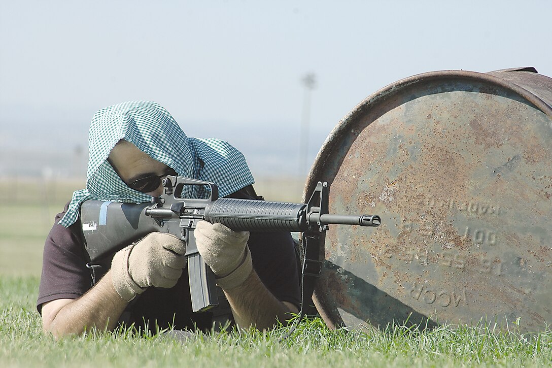 The "enemy insurgent" uses obstacles close to the ground, such as this metal container, to draw a bead on the combatant Airmen who are advancing on his position. (Photo by Senior Airman Joshua Moshier)