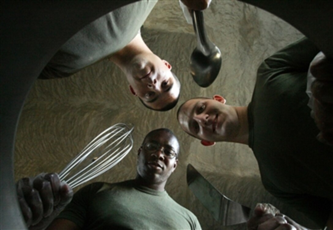 Food service specialists with 3rd Battalion, 2nd Marine Regiment look into a cooking pot at Observation Post Falcons, Iraq, Sept. 23, 2006. The self-proclaimed "combat cooks" brought a chow hall to the field so Marines could have a hot meal. 