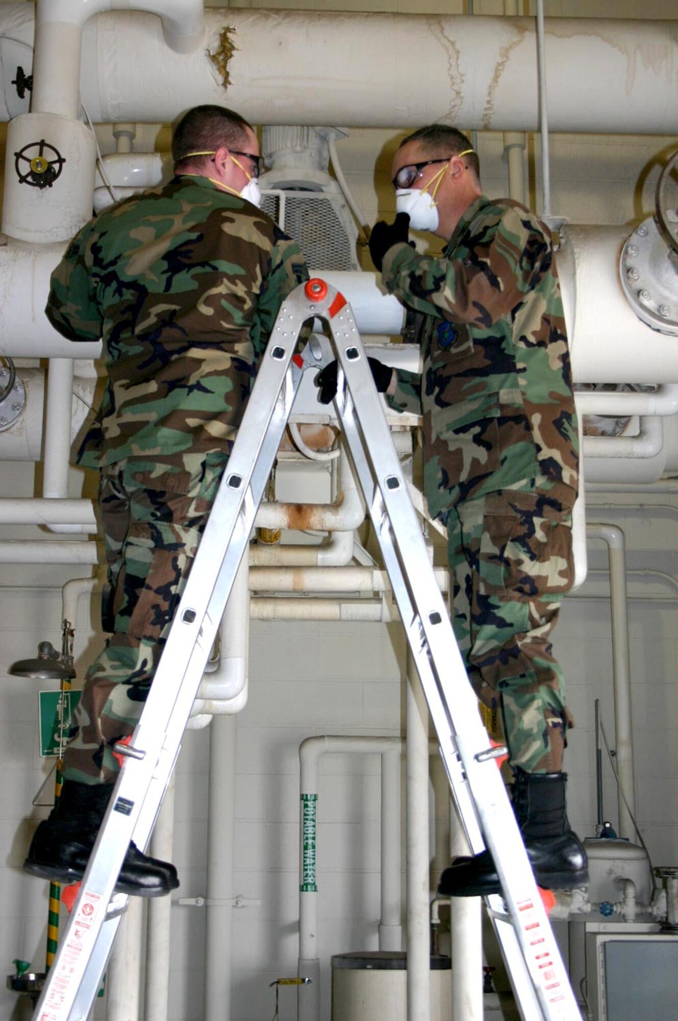 Airman 1st Class Christopher Felton (left) and Col. Rick Martin save energy by installing pipe insulation on a high-temperature water line March 22 in a hangar at McGuire Air Force Base, N.J.  Colonel Martin is the 305th Air Mobility Wing commander and Airman Felton is with the 305th Civil Engineer Squadron.  (U.S. Air Force photo)