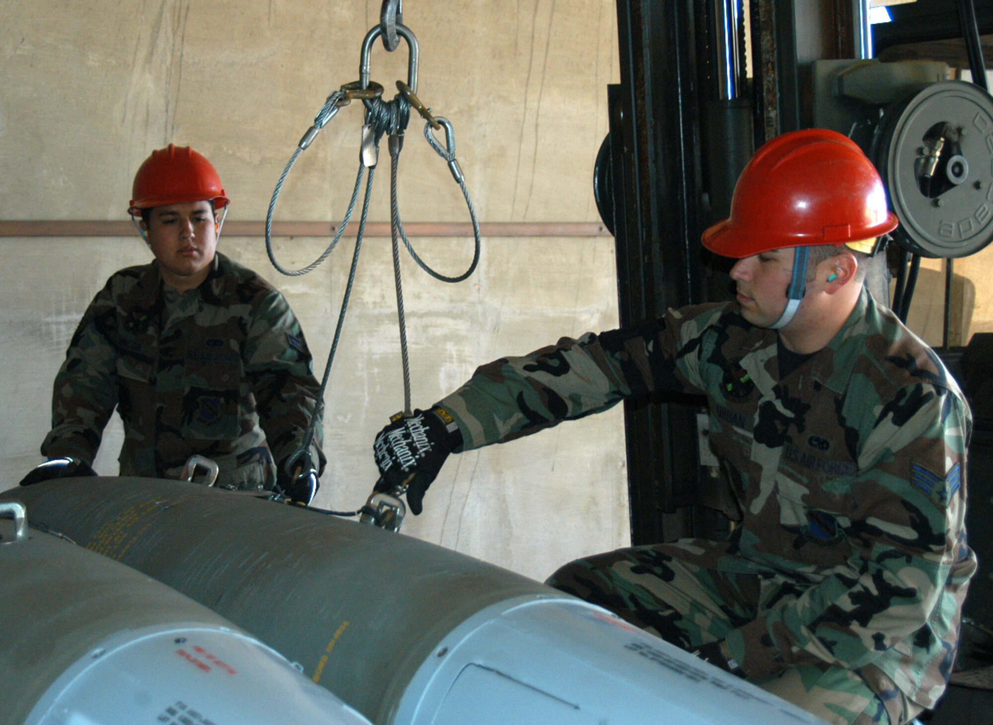 Airman 1st Class Gilbert Rincon (left) and Senior Airman Richard Urban, 7th Munitions Squadron, prepare a live bomb to be loaded on a tractor-trailer and taken to the flightline using proper personal protective equipment April 10. Their attention to detail and care for live munitions contributed to the unit's 2006 Air Force Missile Safety Award. (U.S. Air Force photo by Airman 1st Class Carolyn Viss)