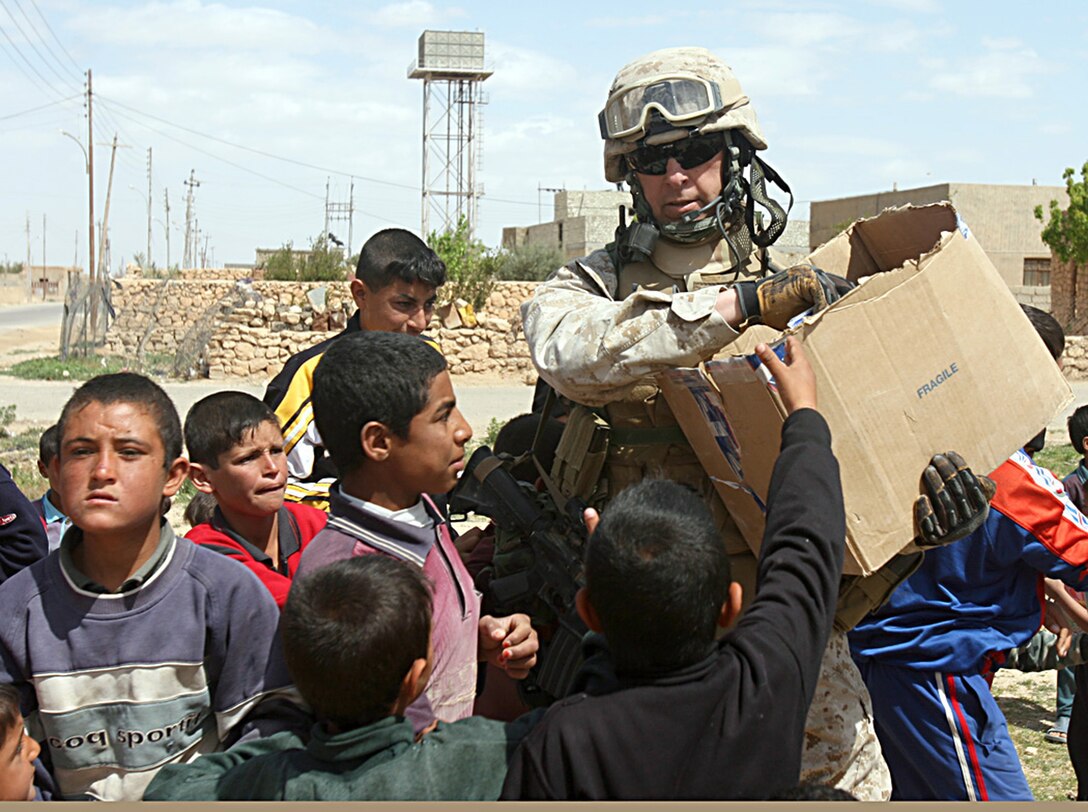 U.S. Marine Sgt. Maj. James C. Burnett, battalion sergeant major with the 1st Light Armored Reconnaissance Battalion, Regimental Combat Team 2, hands clothing and school supplies to children of Anah, Iraq, March 27, 2007.
