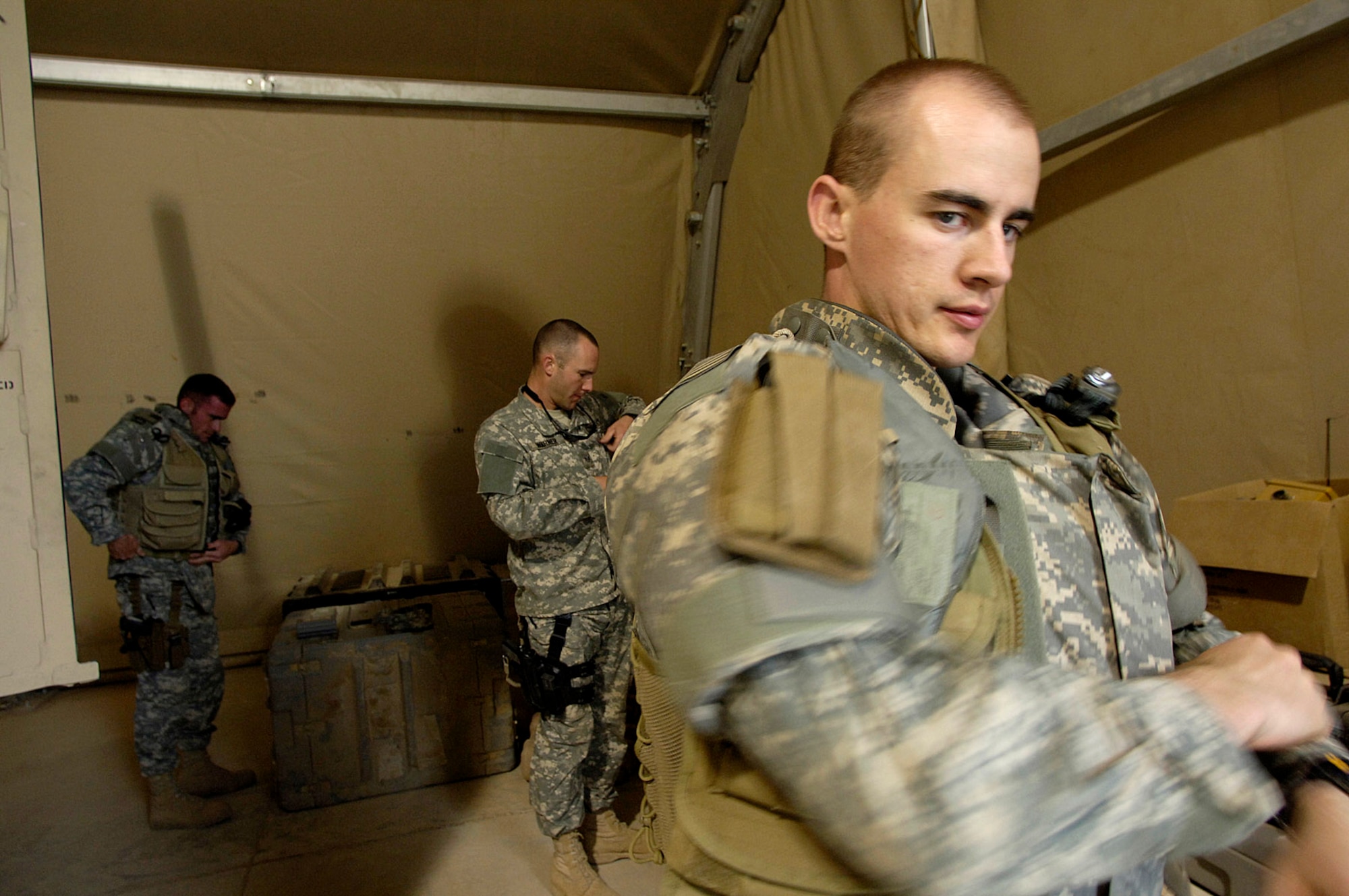 Senior Airman William Newman dons his protective equipment prior to an "outside the wire" mission April 3 at Balad Air Base, Iraq. Airmen Newman is deployed from the Hickam Air Force Base, Hawaii. In background are Staff Sgt. Charles Warner and Staff Sgt. Tom Pilla both deployed from Ramstein Air Base, Germany. The Airmen are assigned to the 332nd Expeditionary Civil Engineer Squadron's Explosive Ordnance Disposal Flight.  (U.S. Air Force photo/Airman 1st Class Nathan Doza)