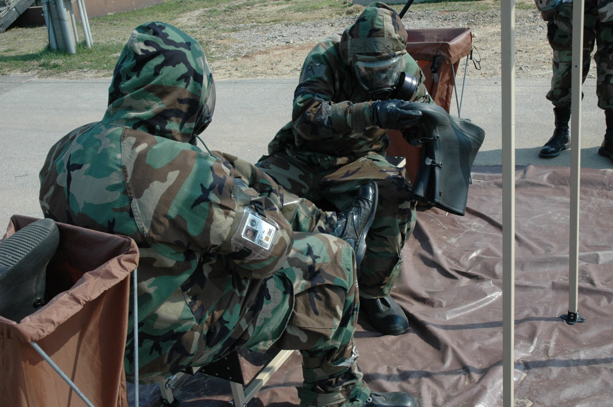 OSAN AIR BASE, Republic of Korea -- Senior Airman Carlos Deleon (right) helps Senior Airman Jung Jun, both 51st Comptroller Squadron, take off a protective over boot while learning to process through a contamination control point at the ATSO Rodeo Friday. (U.S. Air Force photo by Senior Airman Brok McCarthy)