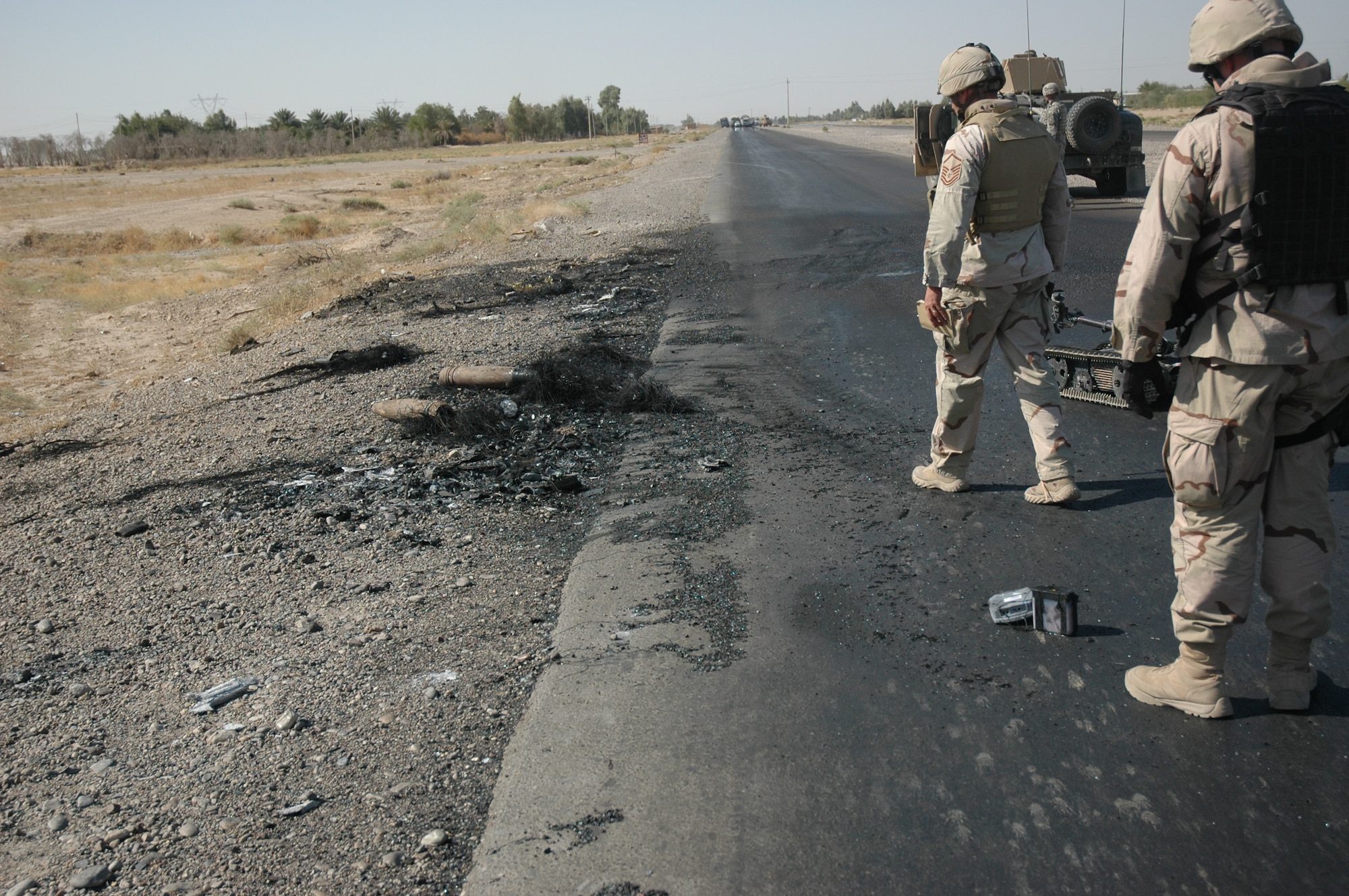 PALIWODA, Iraq -- Waiting for Explosive Ordinance Disposal to confirm the scene is safe, Staff Sgt Christopher Hawks (left) and Master Sgt Albert Schneider (right), prepare to collect evidence and obtain pictures.  The EOD team from Paliwoda and Schneider's Weapons Intelligence Team had just arrived at the scene of two Improvised Explosive Devices detonations targeting civilian vehicles on Main Supply Route Tampa.  (Courtesy photo)