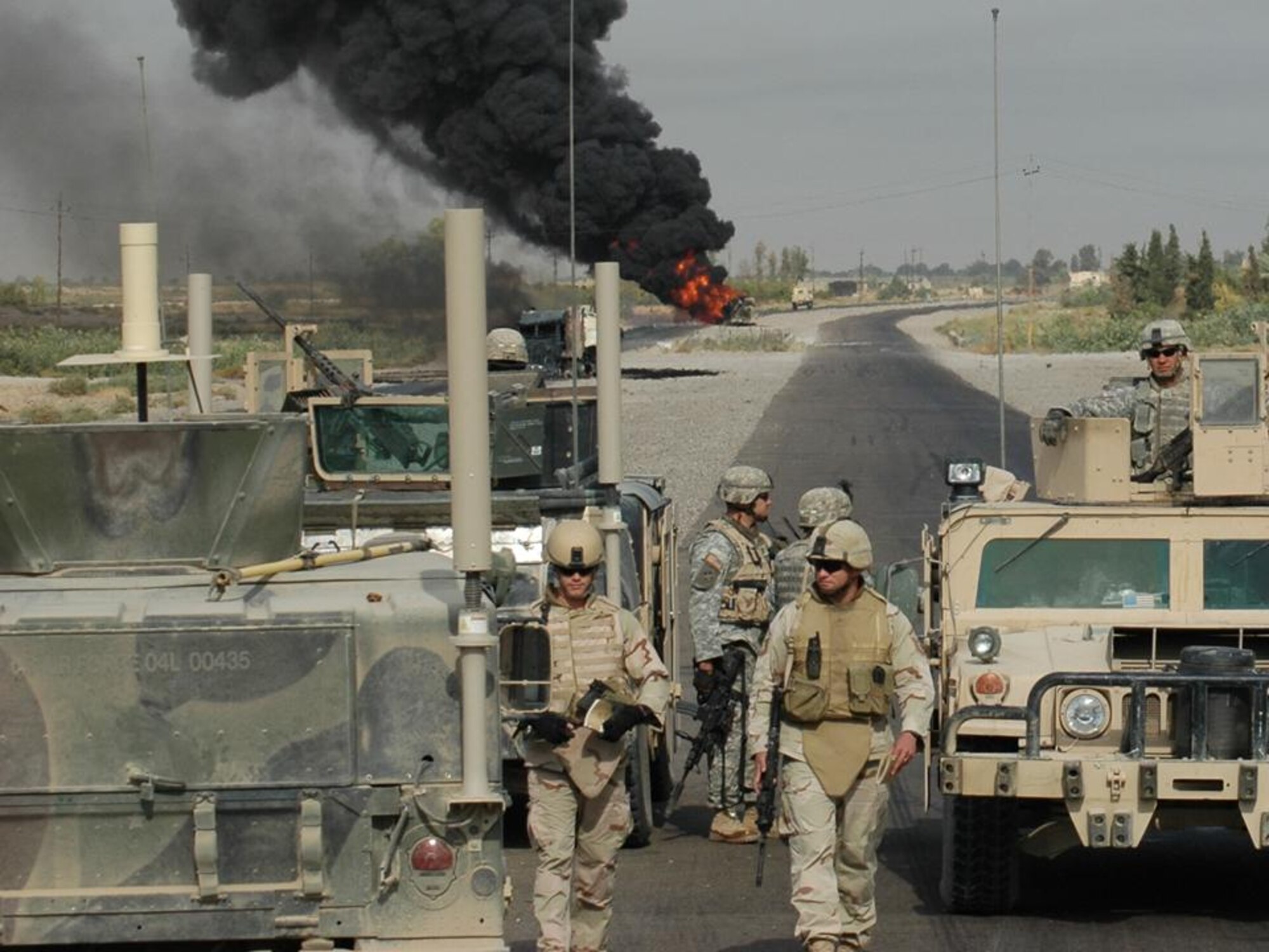 PALIWODA, Iraq -- Waiting for Explosive Ordinance Disposal to confirm the scene is safe, Staff Sgt Christopher Hawks (front left) and Master Sgt Albert Schneider (front right), prepare to collect evidence and obtain pictures.  The EOD team from Paliwoda and Schneider's Weapons Intelligence Team had just arrived at the scene of two Improvised Explosive Devices detonations targeting civilian vehicles on Main Supply Route Tampa.  (Courtesy photo)