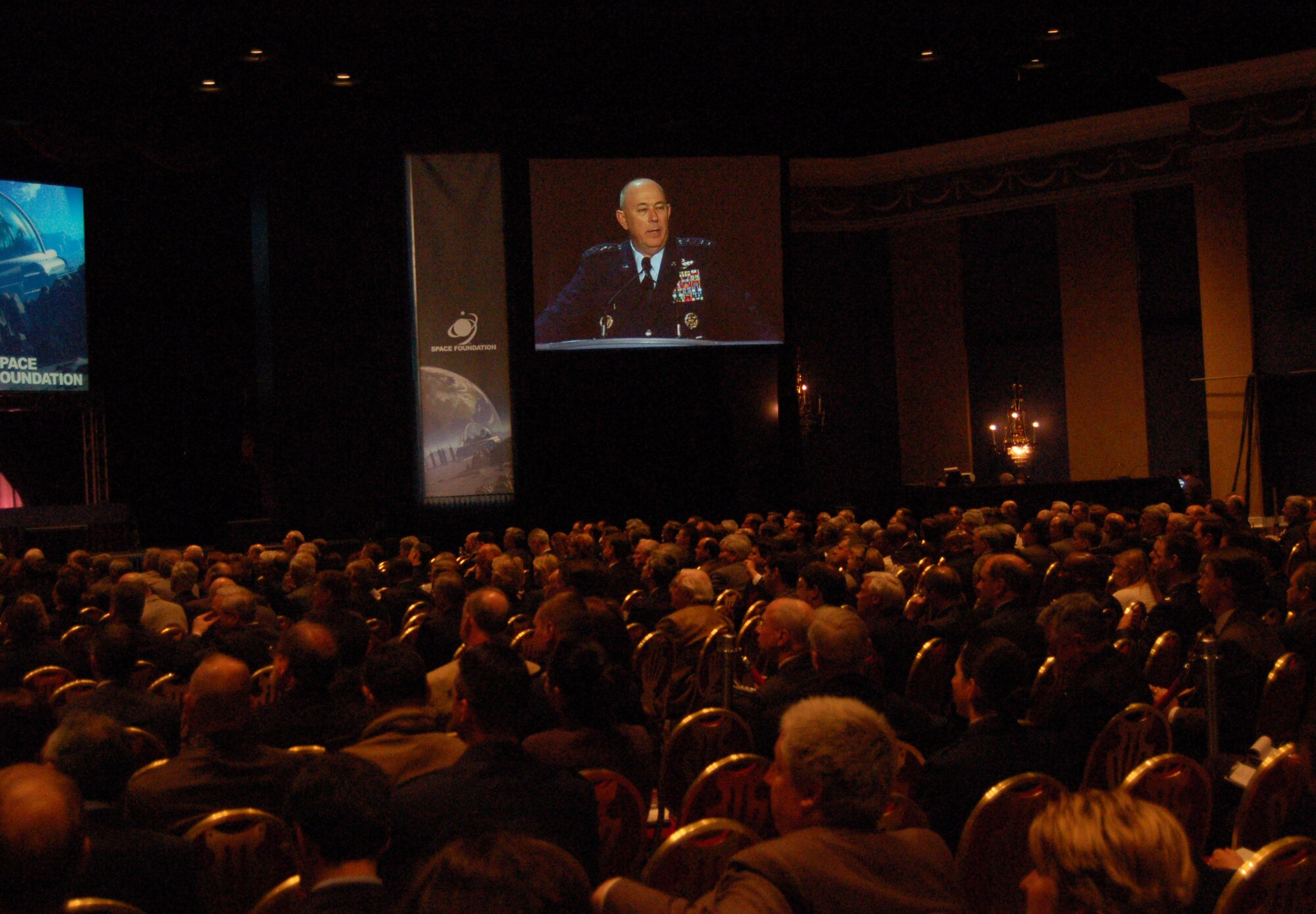 A video of Air Force Chief of Staff Gen. T. Michael Moseley delivering his speech is projected into a corner of an exhibit hall during the 23rd National Space Symposium April 11 at the Broadmoor in Colorado Springs, Colo. The general spoke to a crowd of more than 400 military, civilian and industry space professionals. (U.S. Air Force photo/Staff Sgt. Jeremy Larlee) 