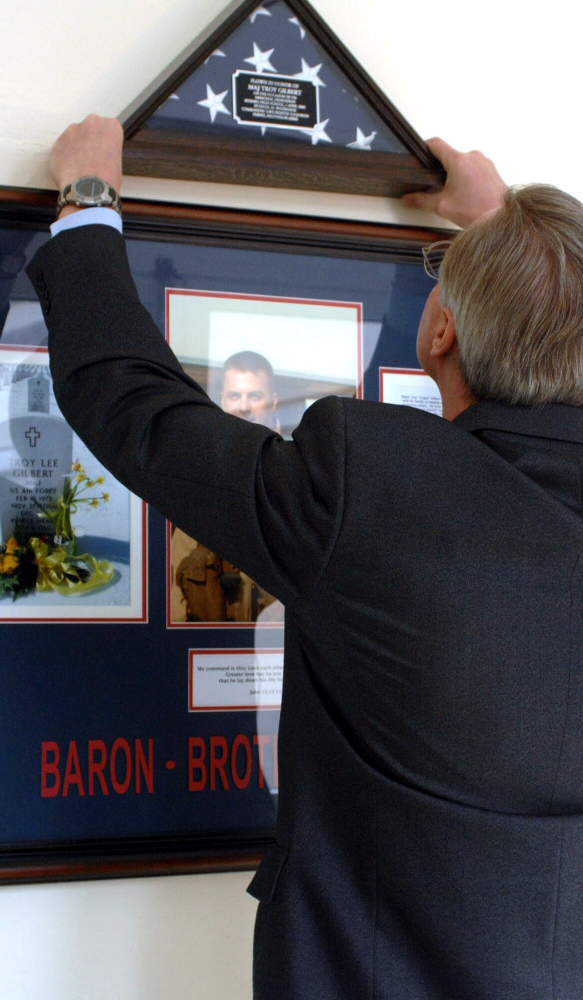 David Carlisle hangs a flag above a commemorative plaque hung in the memory of Maj. Troy Gilbert April 5 at Bitburg High School near Spangdhalem Air Base, Germany. Major Gilbert was a BHS graduate. He was supporting Operation Iraqi Freedom when he lost his life when his F-16 Fighting Falcon crashed Nov. 27, 2006, 20 miles northwest of Baghdad. Major Gilbert was on a mission providing combat support to both an Army helicopter crew that had crashed and ground forces trying to reach the crash site in the Anbar Province, 20 miles northwest of Baghdad. Mr. Carlisle is the Bitburg High School principal. (U.S. Air Force photo/Airman 1st Class Emily Moore) 
